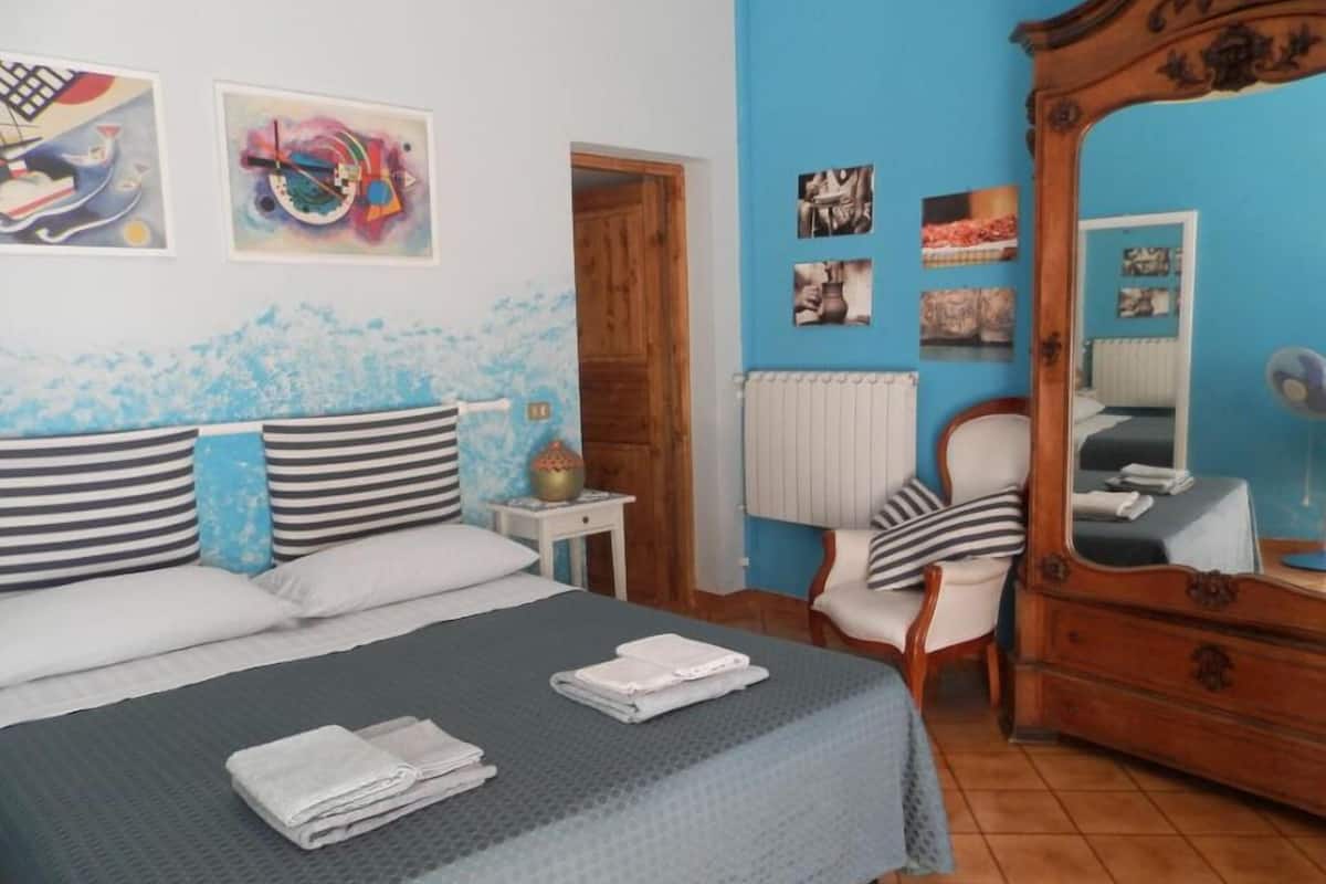 A bedroom with a bed, a chair, a dresser, and wall art.