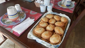 Spisebord med en bakke friskbagte rundstykker, kaffemaskine og diverse køkkenartikler.