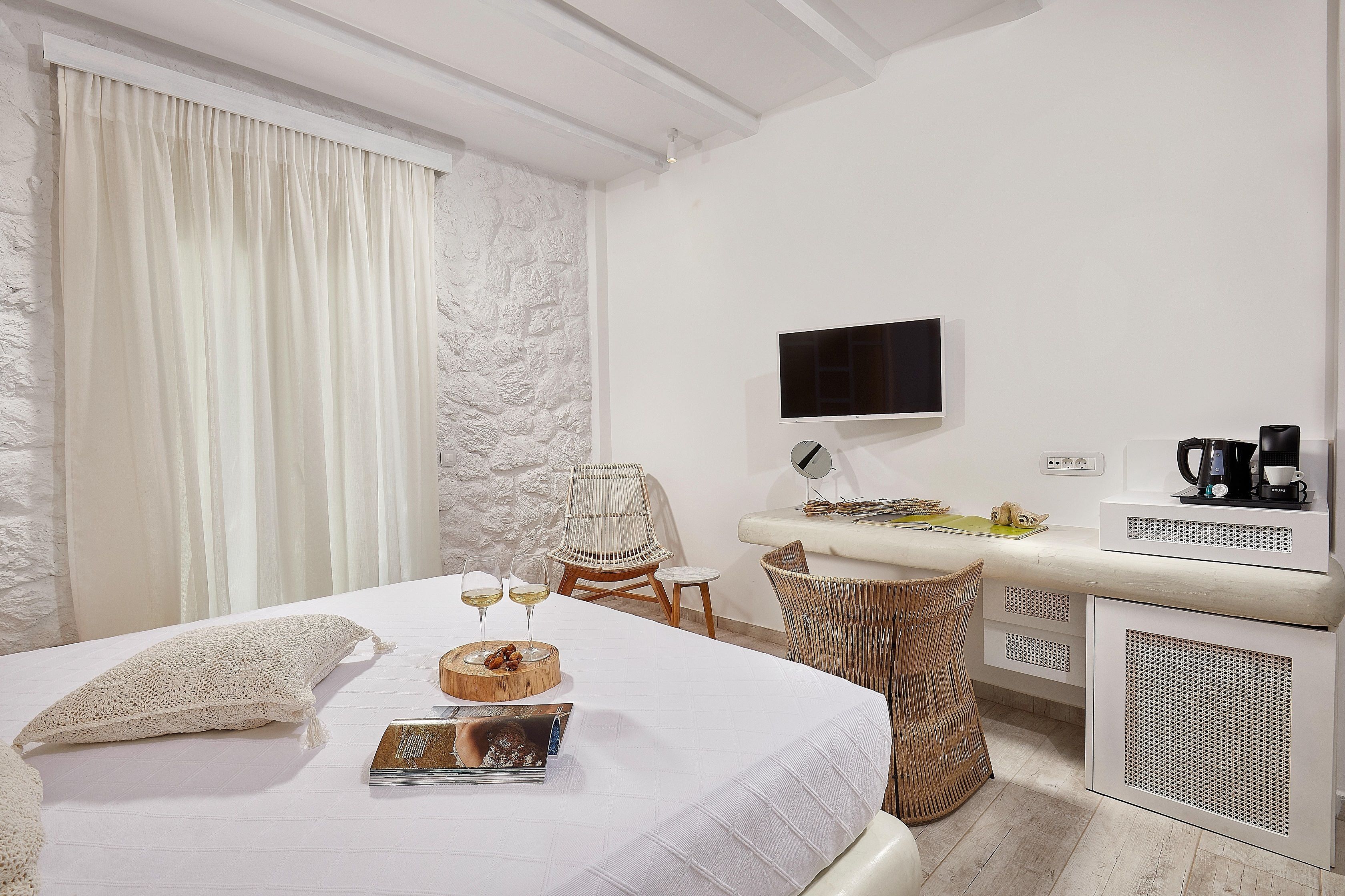 A hotel room with a bed, a desk with a flat-screen TV, a coffee maker, and a wicker chair.