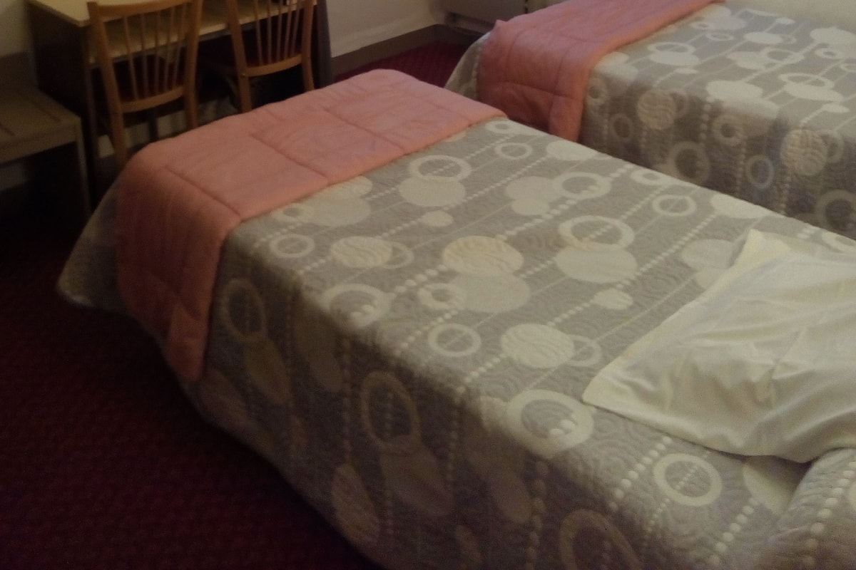 A hotel room with two beds, a desk, a chair, a television, and a window with curtains.