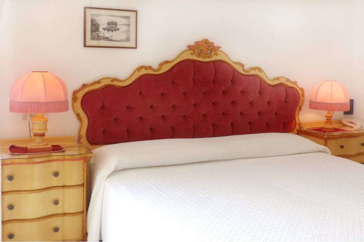 A neatly made bed with a red upholstered headboard, two bedside tables with lamps, and a framed picture on the wall.