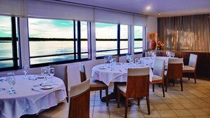 A restaurant with tables set for dining, large windows with a view of the water, and a decorative wall with vertical lines. - Jungle Experiences La Perla (Nauta)