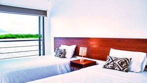 A hotel room with two beds, a wooden headboard, a nightstand with a lamp, and a large window offering a view of the beach. - Jungle Experiences La Perla (Nauta)