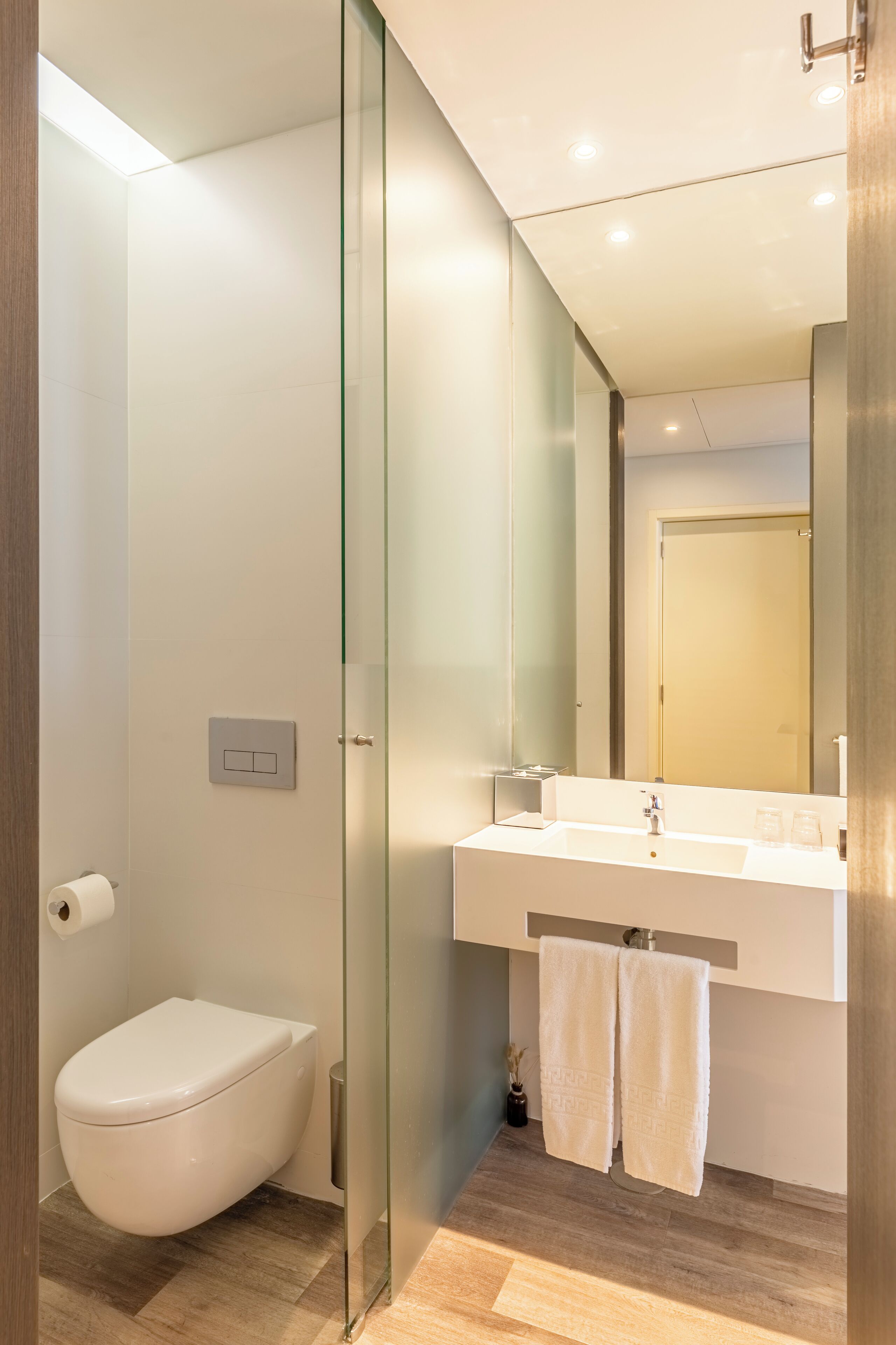 Une salle de bain moderne avec une douche à parois de verre, des toilettes blanches, un lavabo avec un miroir et un porte-serviettes.