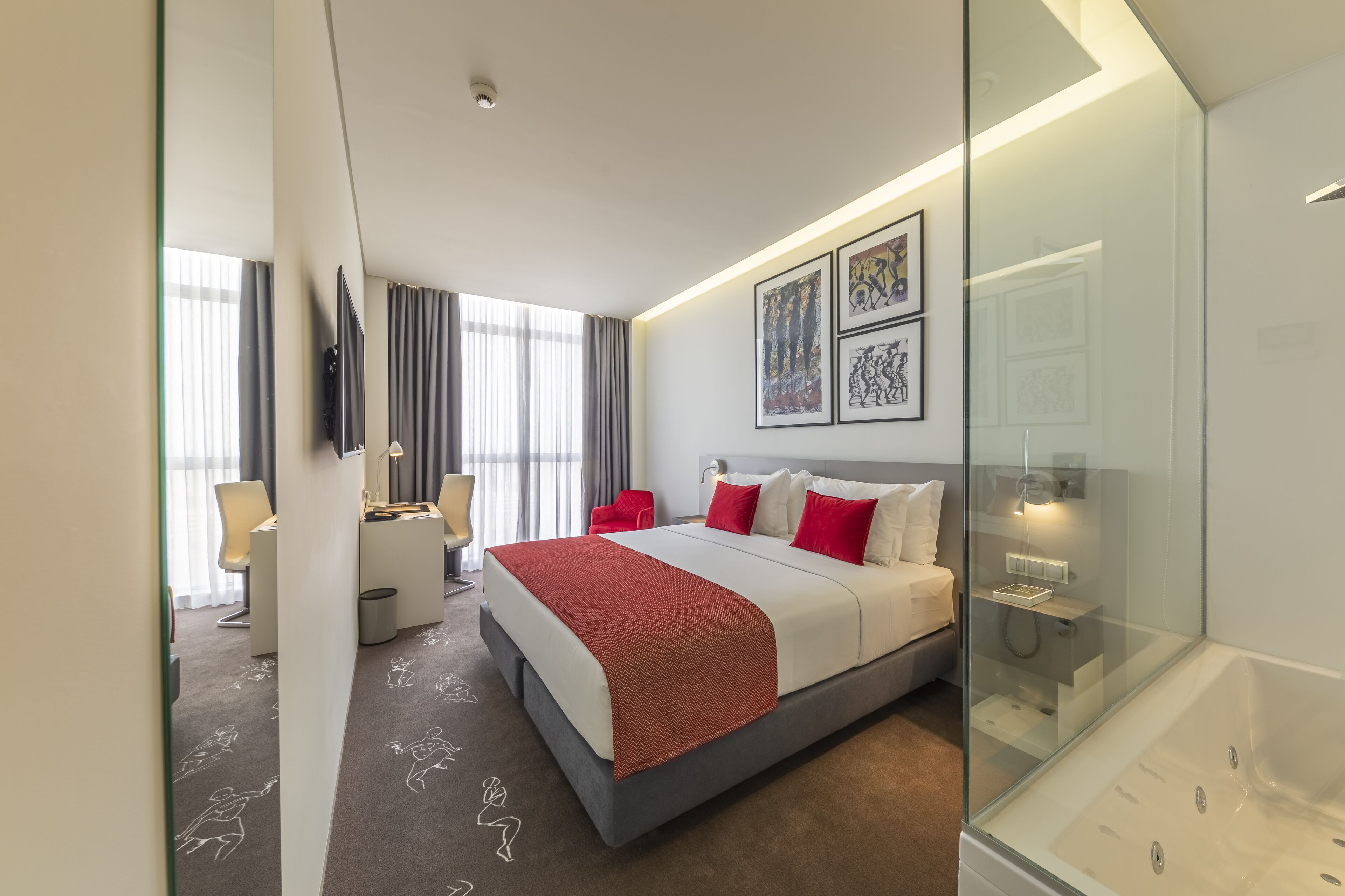 Una habitación de hotel moderna con una cama grande, un escritorio y una bañera de hidromasaje con mampara de vidrio.