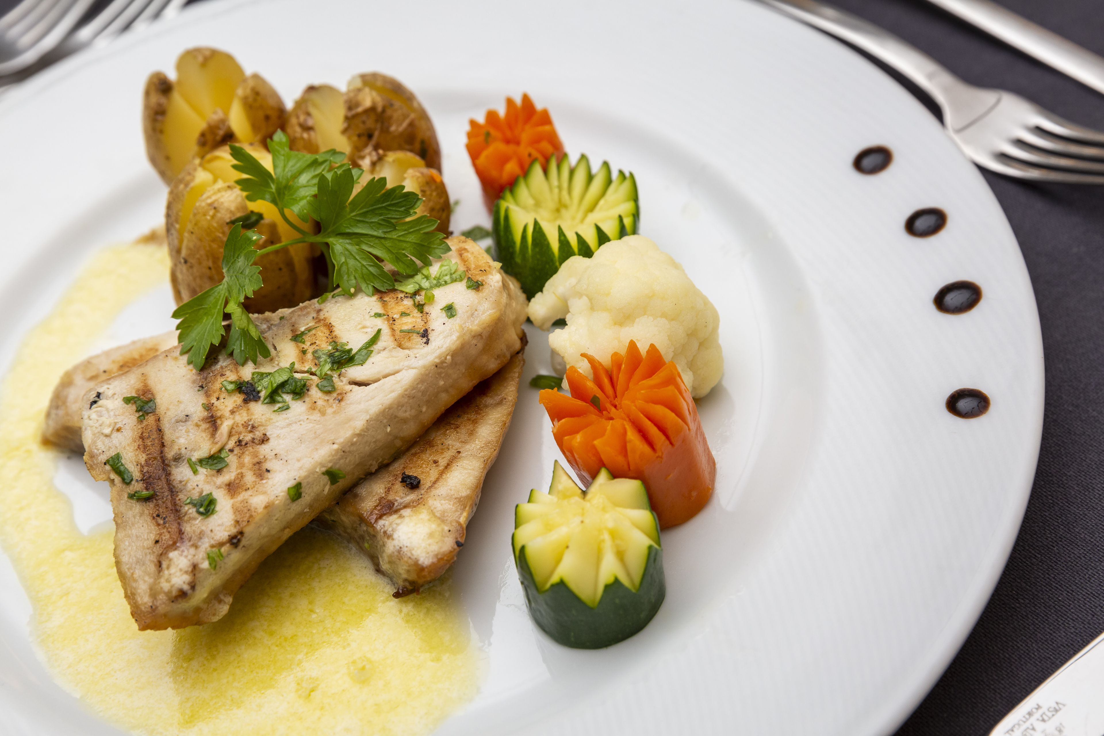 Un plato de comida con un trozo de pescado a la parrilla, patatas y verduras talladas.