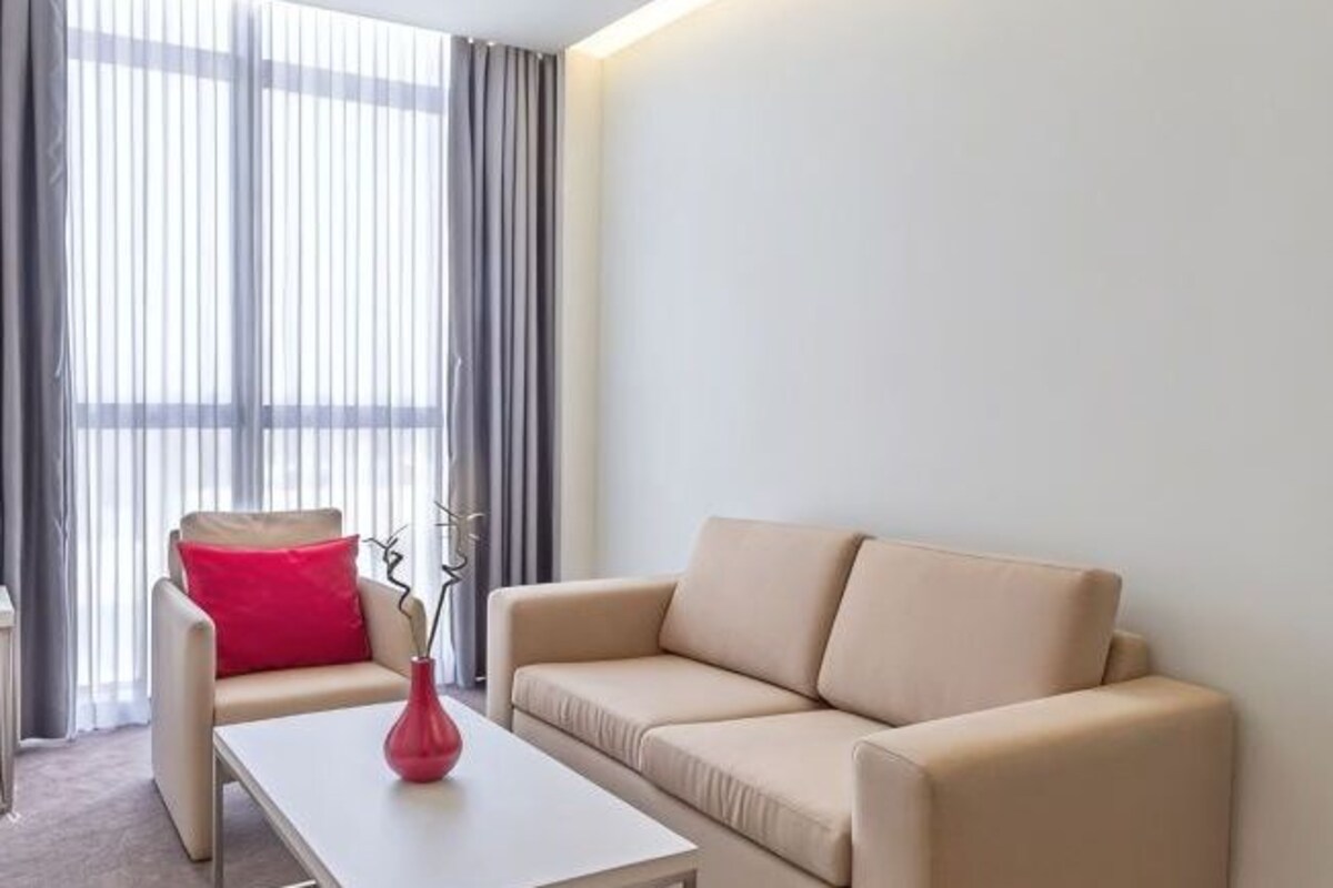A living room with a beige sofa, a red chair, a white coffee table, and a vase with a plant.