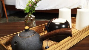 Ein hölzernes Tablett mit einem Teekessel, einer kleinen Vase mit Blumen und zwei Kerzen auf einem Tisch im Hotelzimmer.