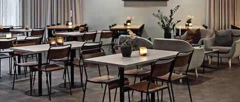 Un comedor moderno con varias mesas y sillas, velas en cada mesa, y un sofá al fondo.