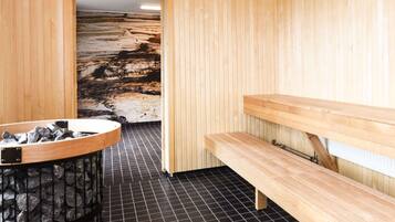Una sauna con una parete a focolare in pietra, panche di legno e pavimento piastrellato.