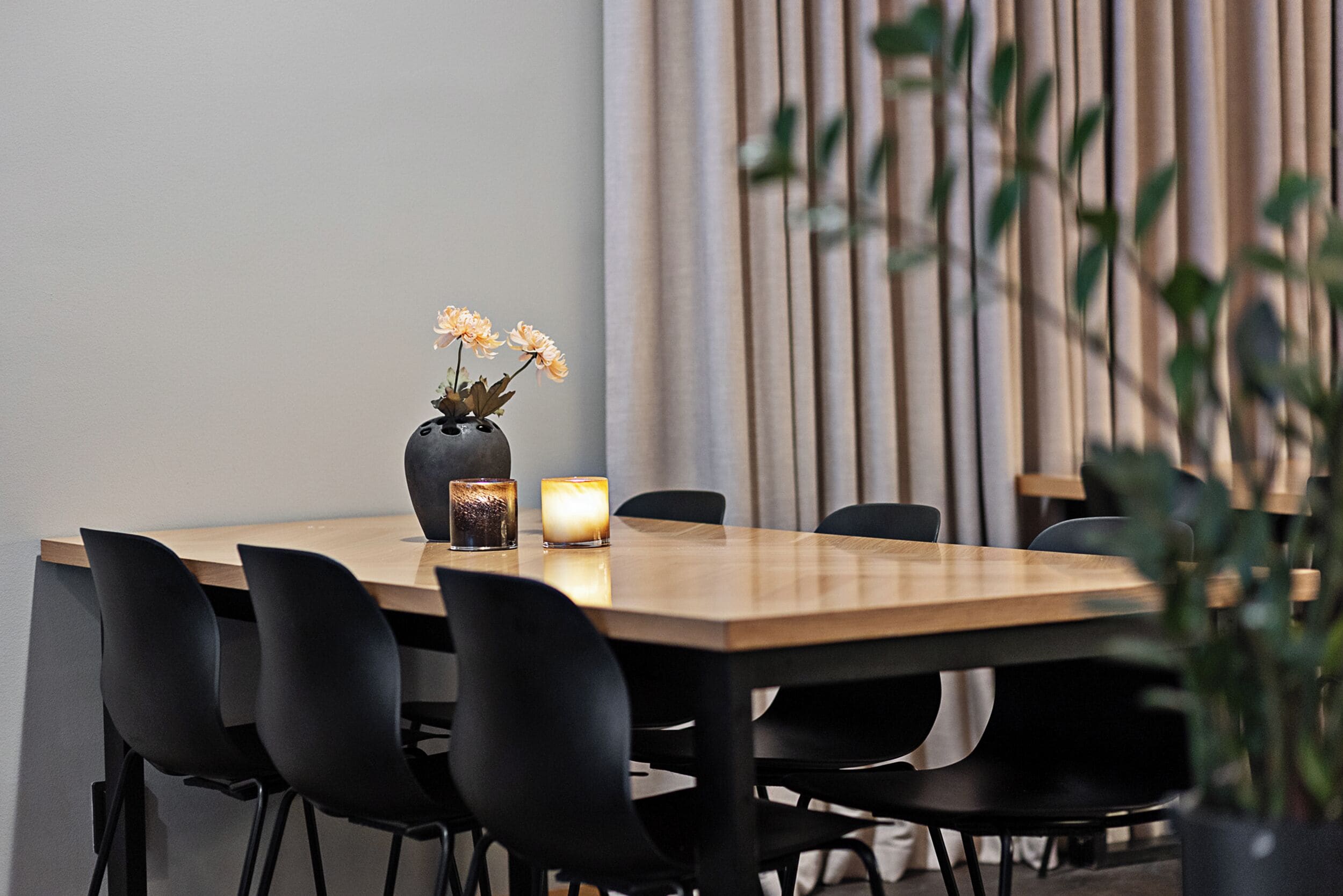 A dining area with a wooden table, black chairs, a vase with flowers, and candles.