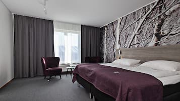 Habitación de hotel con una cama grande, un escritorio, dos sillas y vistas a árboles desde la ventana.