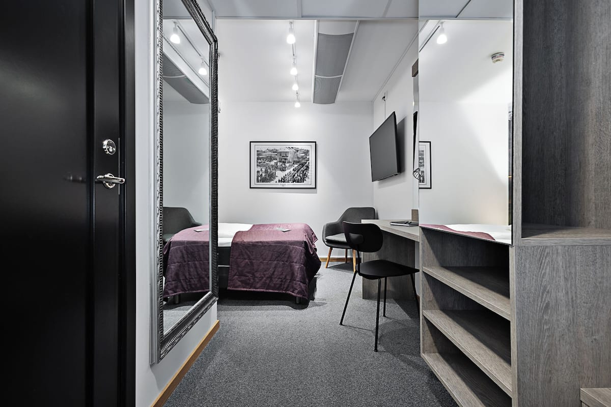 Ett kompakt hotellrum med en säng, ett skrivbord, en stol och en garderob.