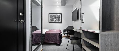 A compact hotel room with a bed, a desk, a chair, and a wardrobe.
