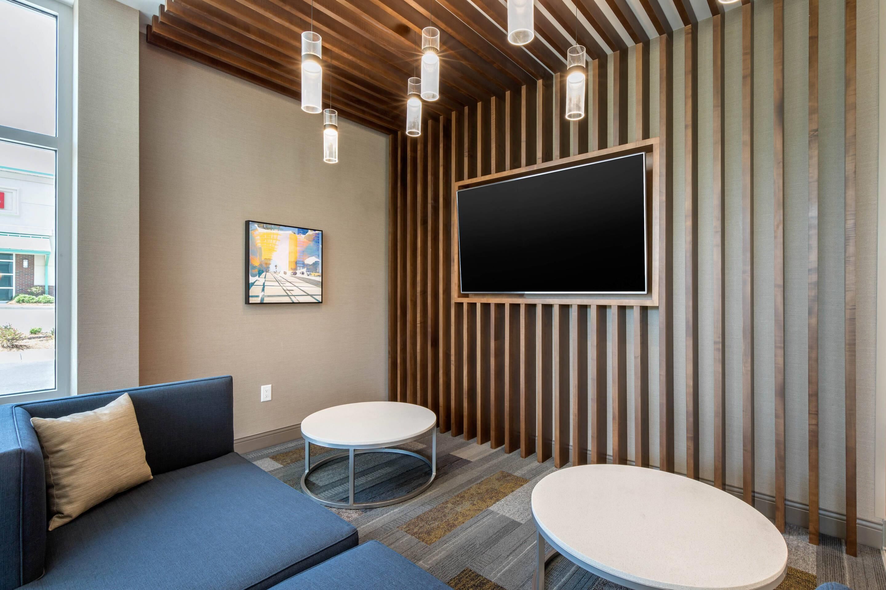 Un espace d’attente moderne avec un canapé bleu, deux tables rondes, un téléviseur fixé au mur et des lambris en bois.