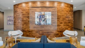 Un hall d’entrée moderne avec un mur en bois aux lignes courbes, un espace salon central doté d’un canapé bleu et une grande œuvre d’art encadrée accrochée au mur.