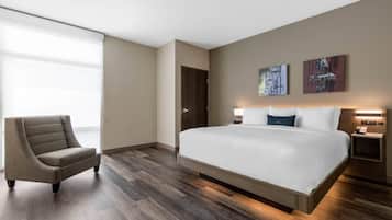 A modern hotel room with a large bed, a chair, a door, and artwork on the wall.