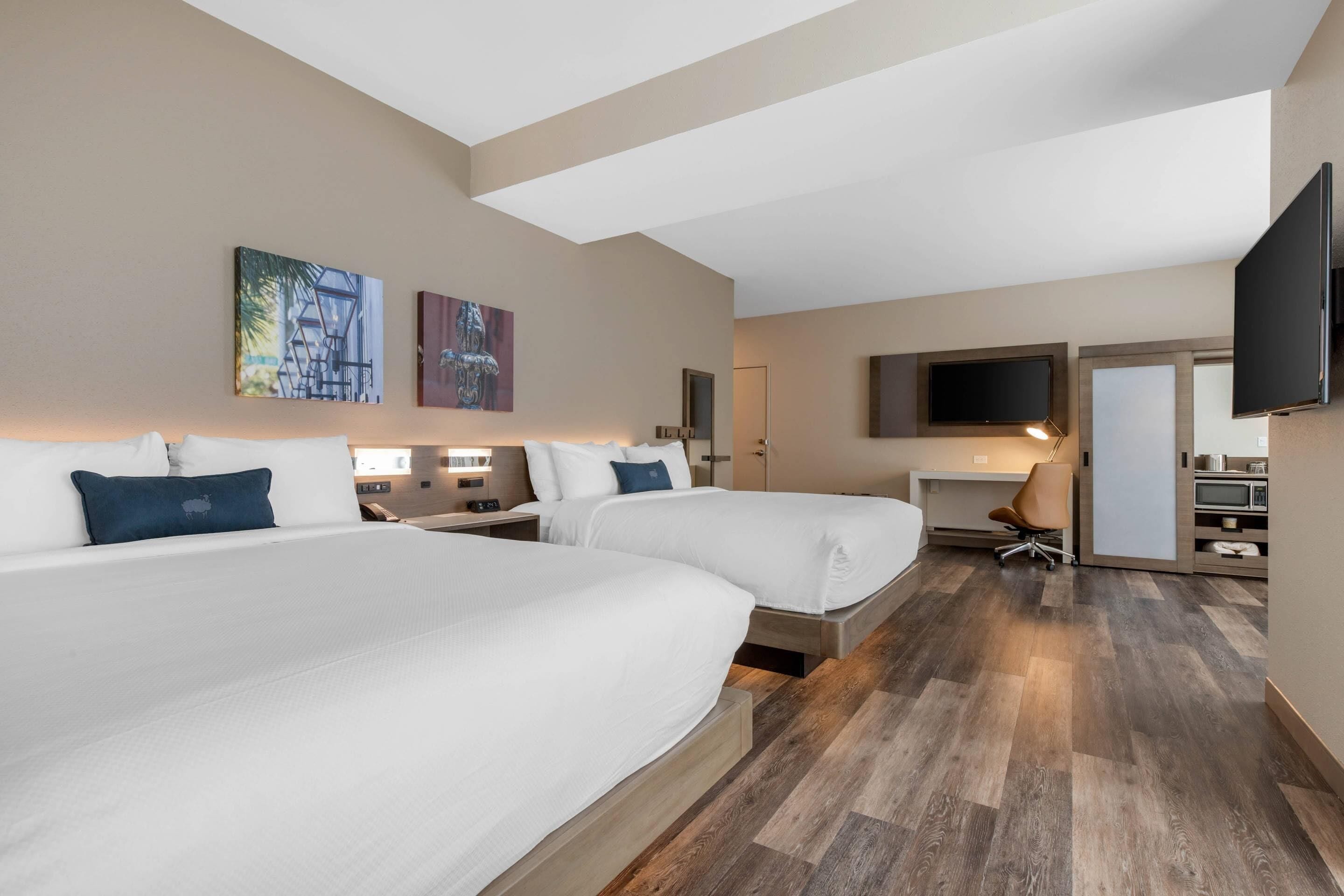 A hotel room with two beds, a desk, a chair, a TV, and artwork on the walls.