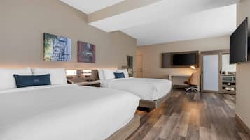 A hotel room with two beds, a desk, a chair, a TV, and artwork on the walls.