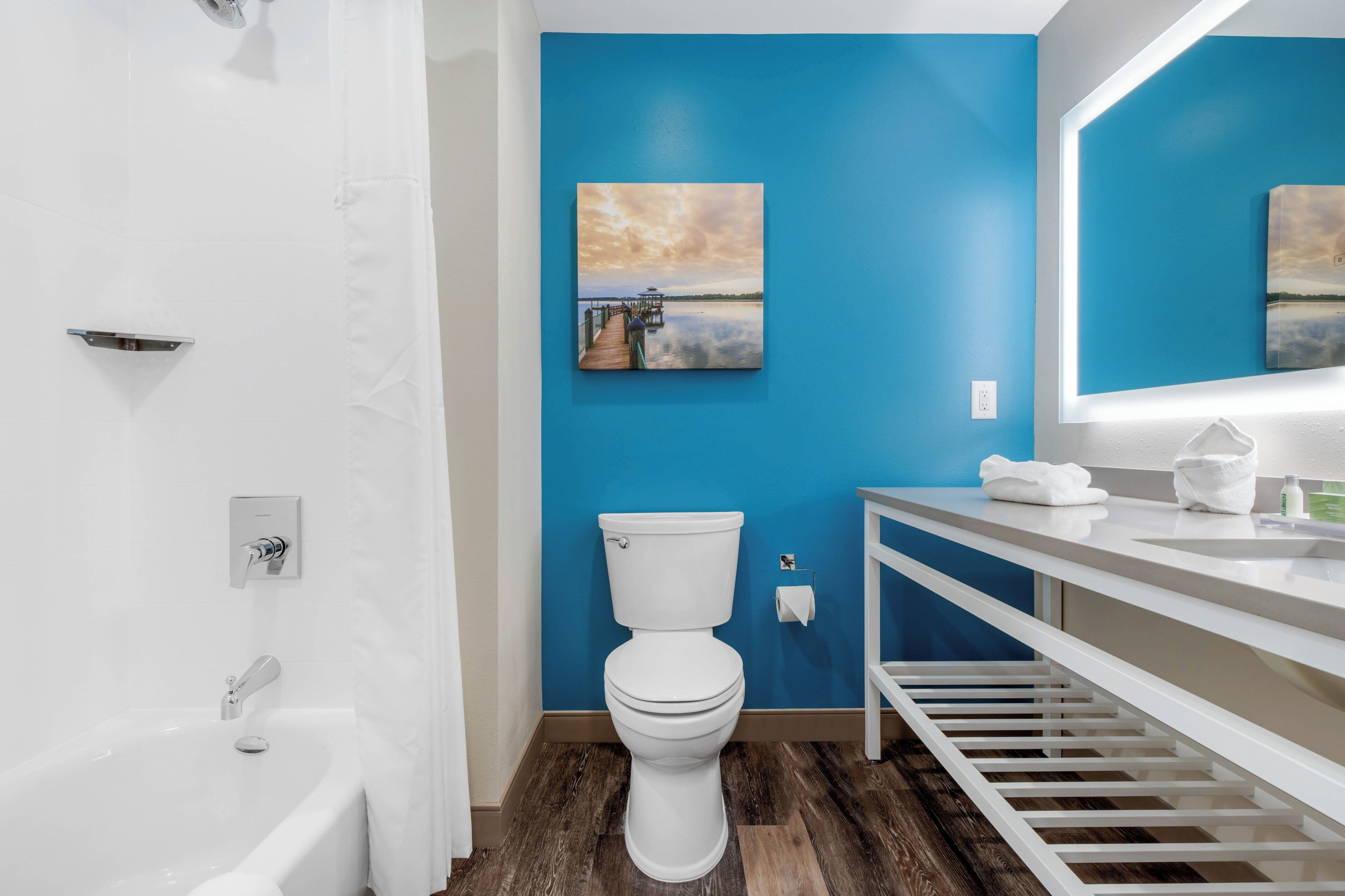 Un baño con inodoro y lavamanos blancos, y suelo de madera.