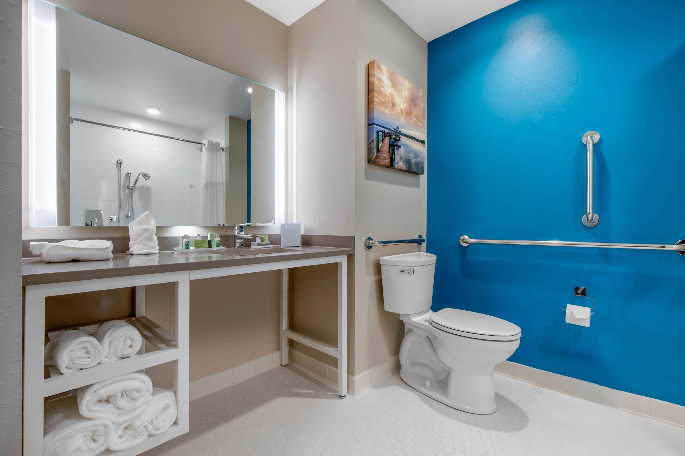 A modern bathroom with a white toilet, a sink with a mirror, and a blue accent wall.