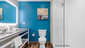 A bathroom with a blue wall, a white toilet, a sink with a mirror, and a shower area.