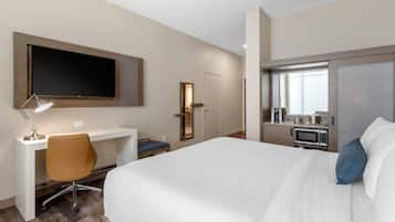 A hotel room with a bed, desk, chair, TV, and kitchenette.