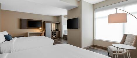 A hotel room with a large bed, a desk, a chair, a TV, and a window with a view.