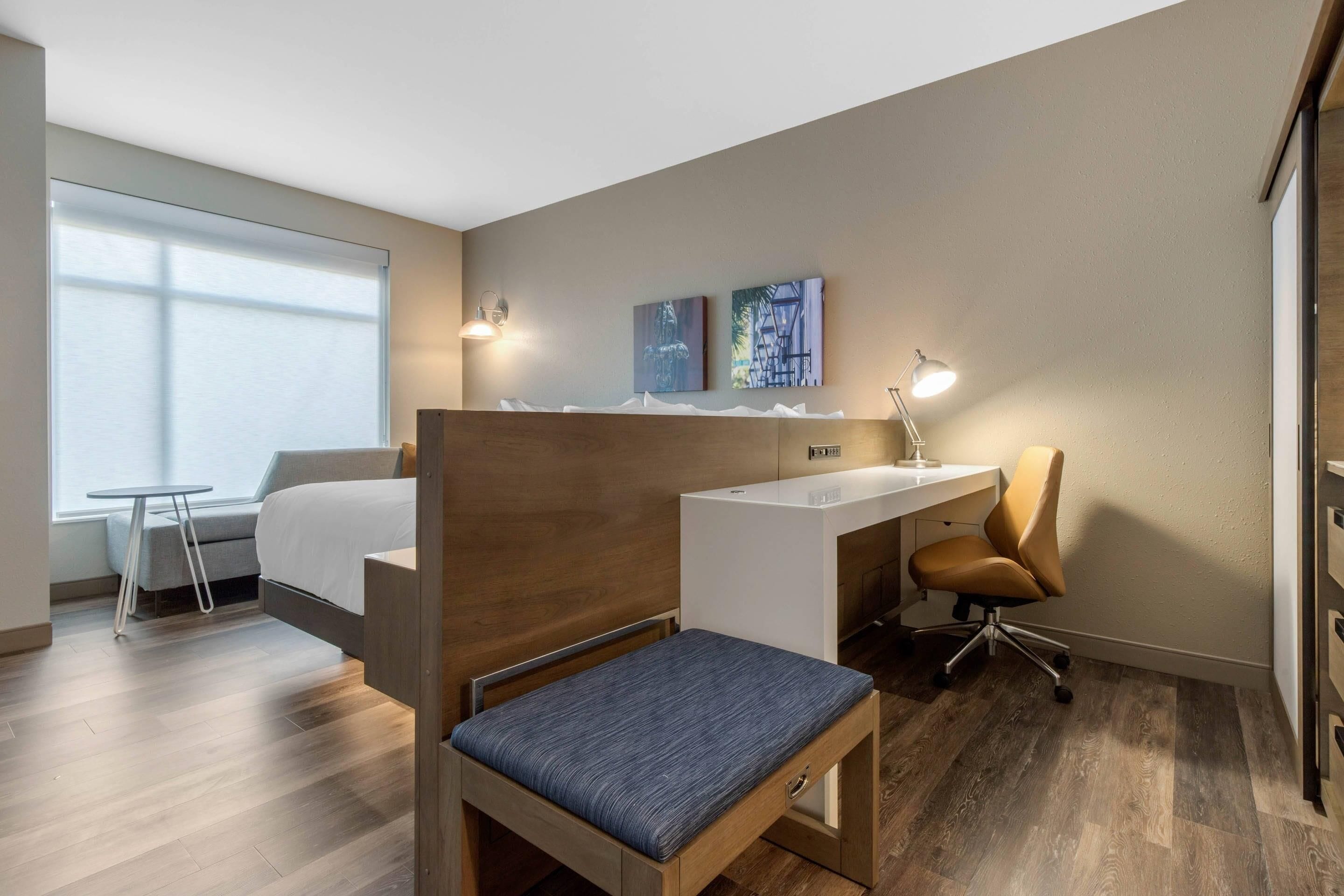 Une chambre d’hôtel avec un lit, un bureau, une chaise, une petite table et des œuvres d’art accrochées au mur.