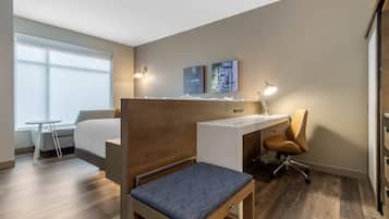 A hotel room with a bed, a desk, a chair, a small table, and artwork on the wall.