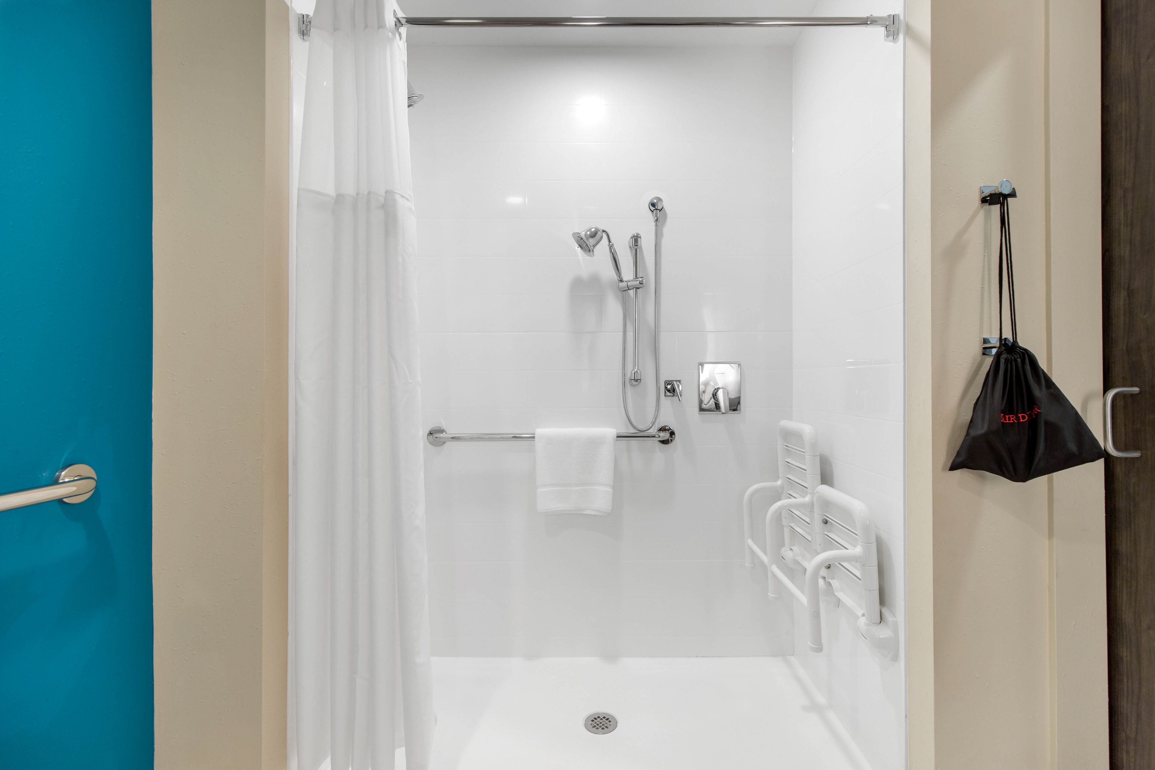 A modern shower area with a glass door, a towel rack, and a black bag hanging on the wall.