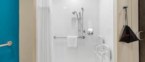 A modern shower area with a glass door, a towel rack, and a black bag hanging on the wall.