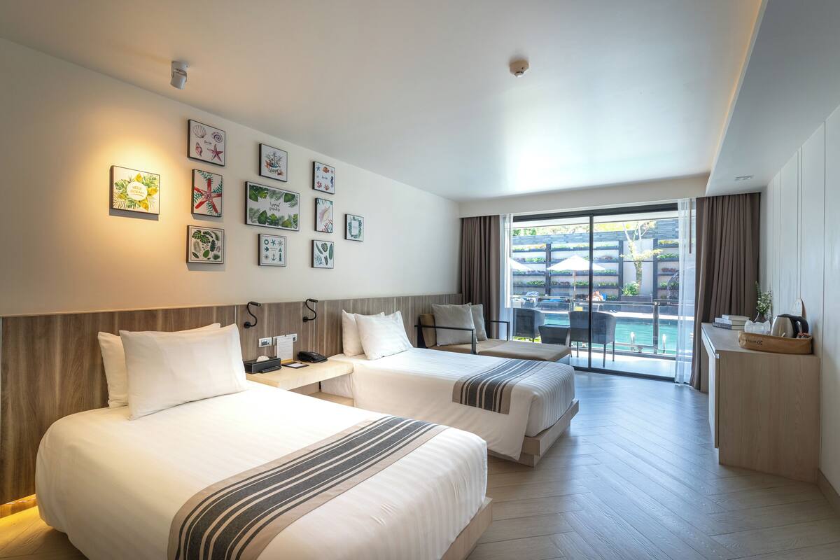 Een hotelkamer met twee bedden, een bureau, een stoel en een balkon met uitzicht op het zwembad.