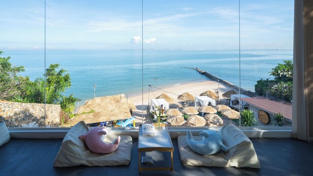 Una habitación con un ventanal grande con vistas a una playa, que incluye un sofá con cojines, una mesita y vista al mar y a la playa.