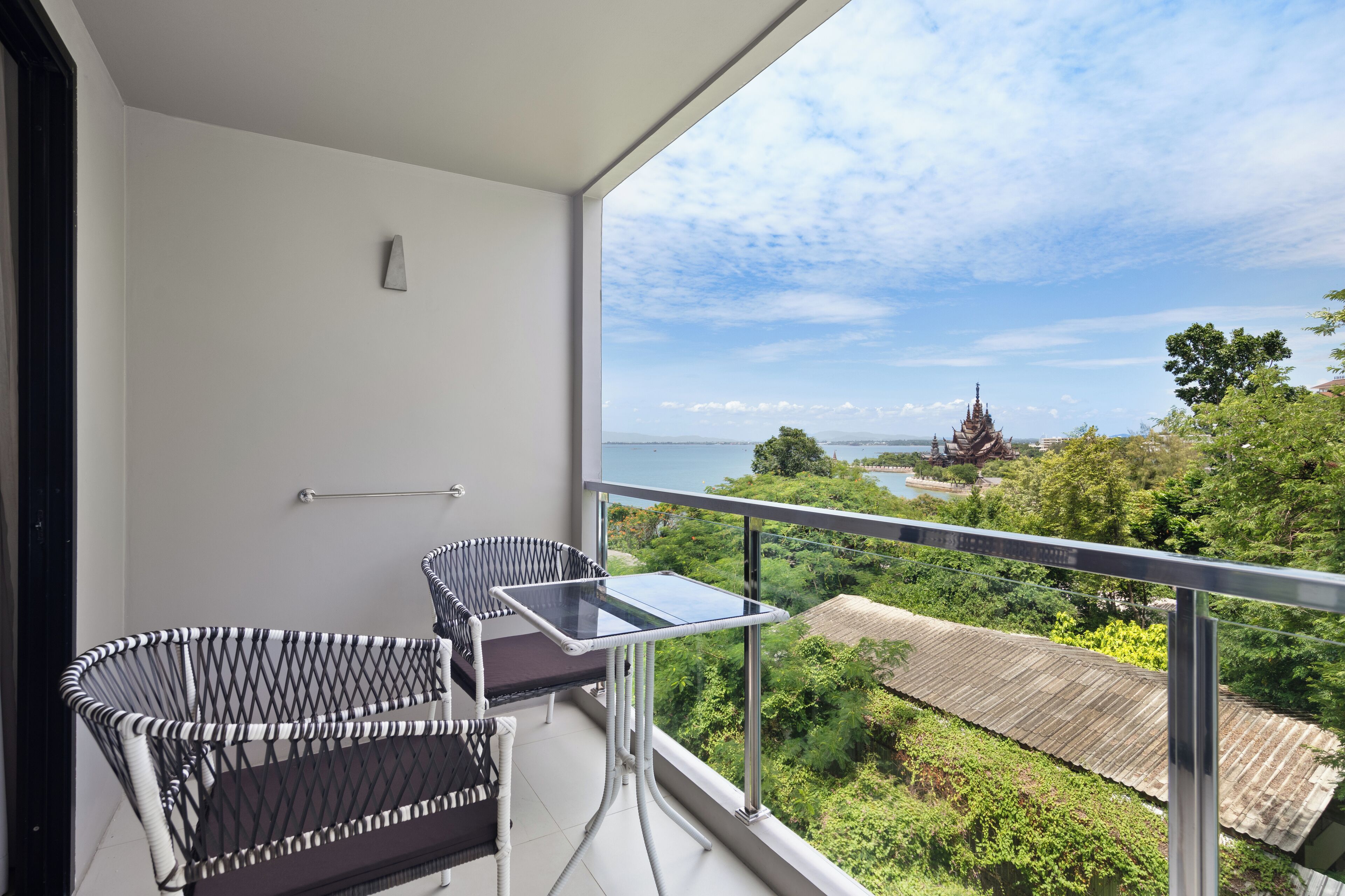Varanda com mobiliário de vime e mesa de vidro, com vista para uma paisagem exuberante e um templo.