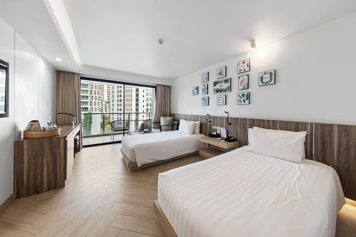 Een moderne hotelkamer met twee bedden, een houten bureau en een balkon met uitzicht op de stad.