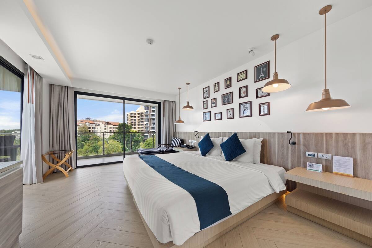 Een moderne hotelkamer met een groot bed, een houten nachtkastje, een bureau en een uitzicht op de skyline door grote ramen.