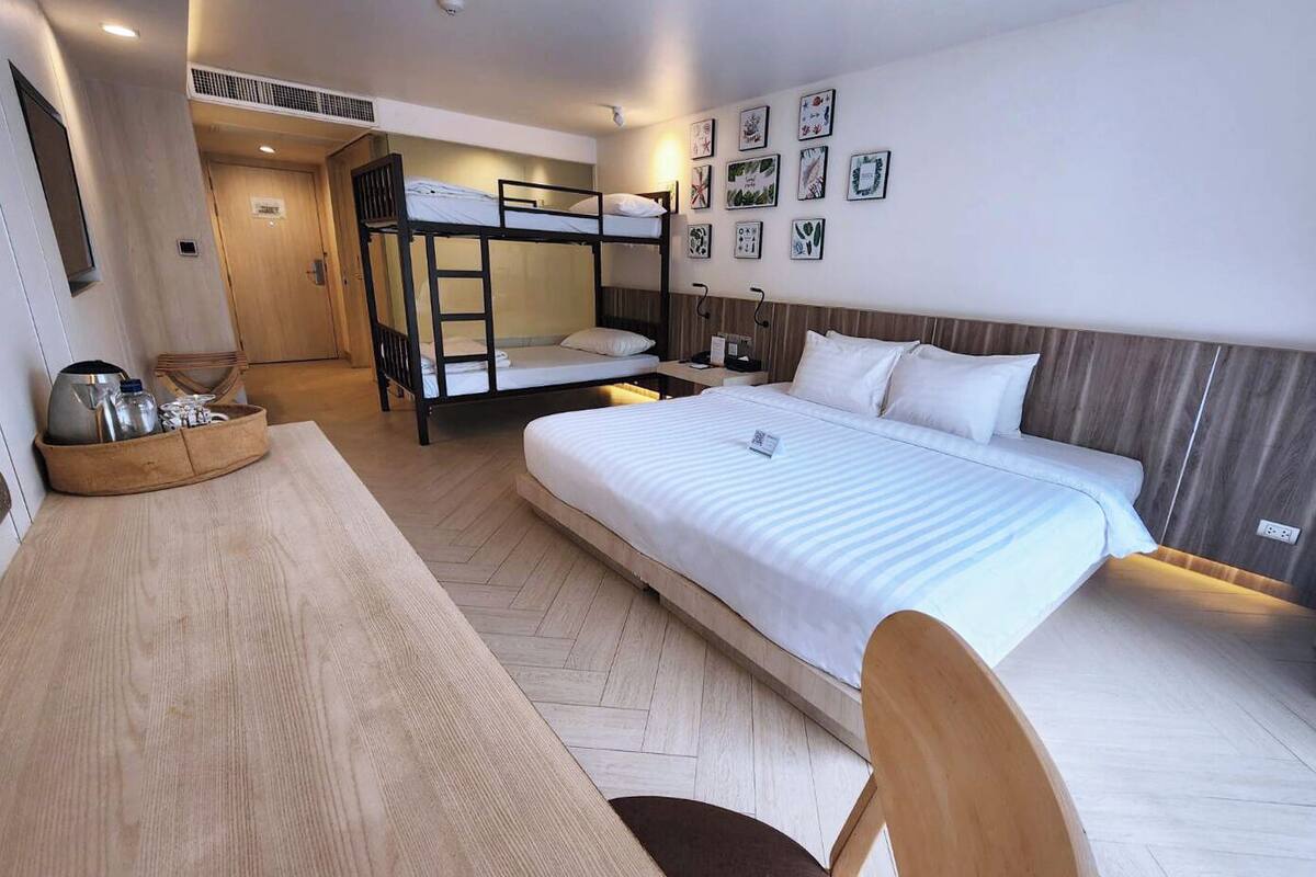 Een hotelkamer met een stapelbed, een eenpersoonsbed, een houten bureau en een stoel.
