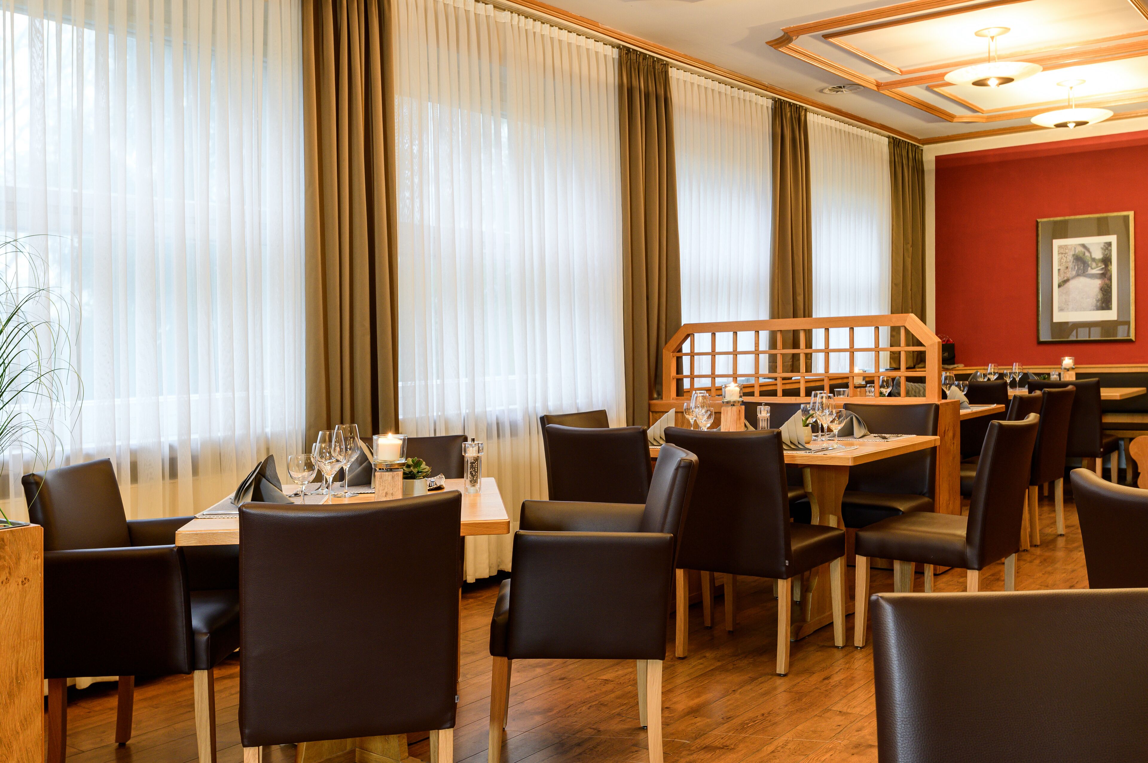 A restaurant with tables and chairs, a wooden staircase, and a red wall with a framed picture.