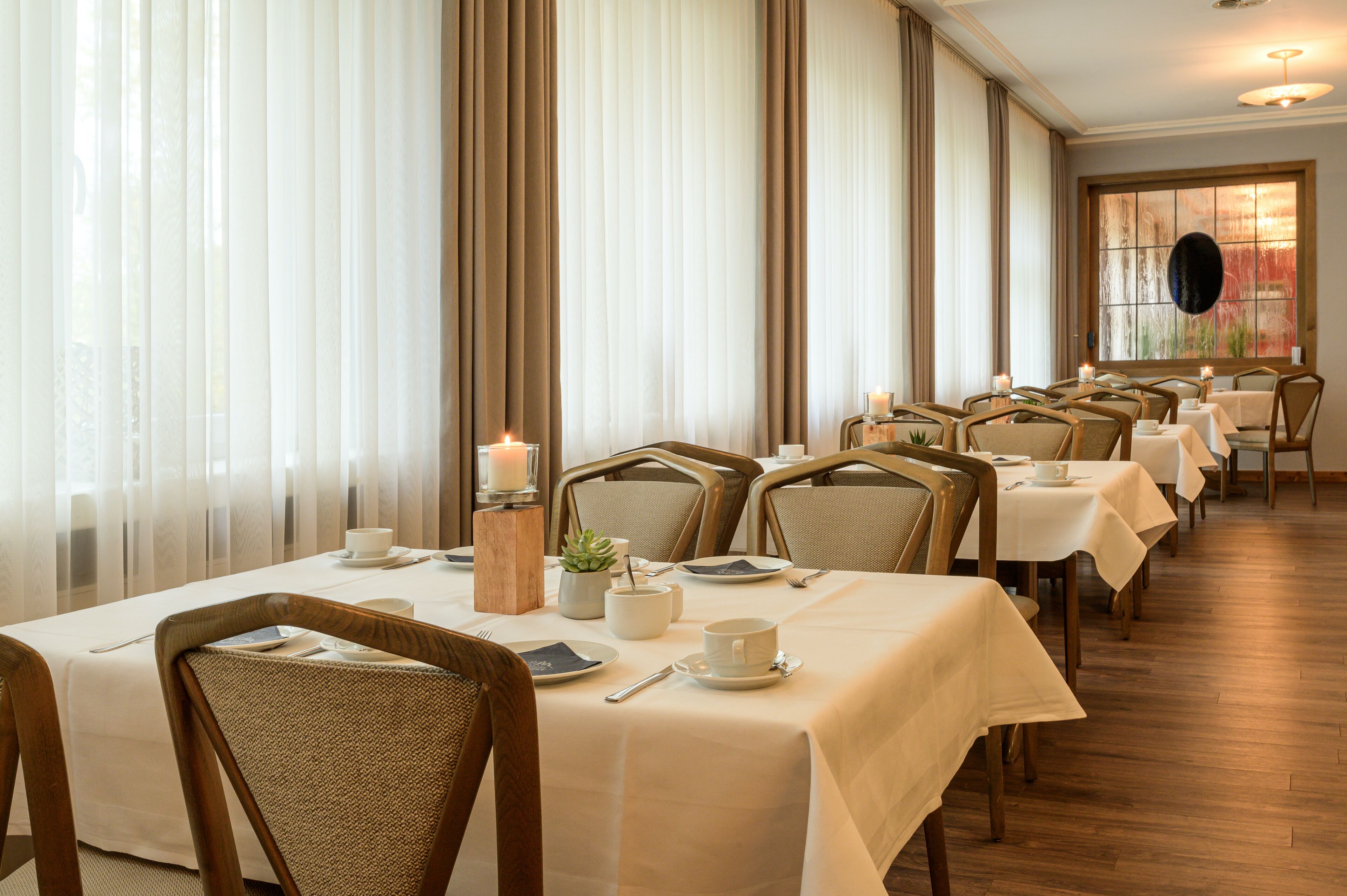 Un comedor con mesas dispuestas para el servicio, con sillas de madera y manteles blancos.