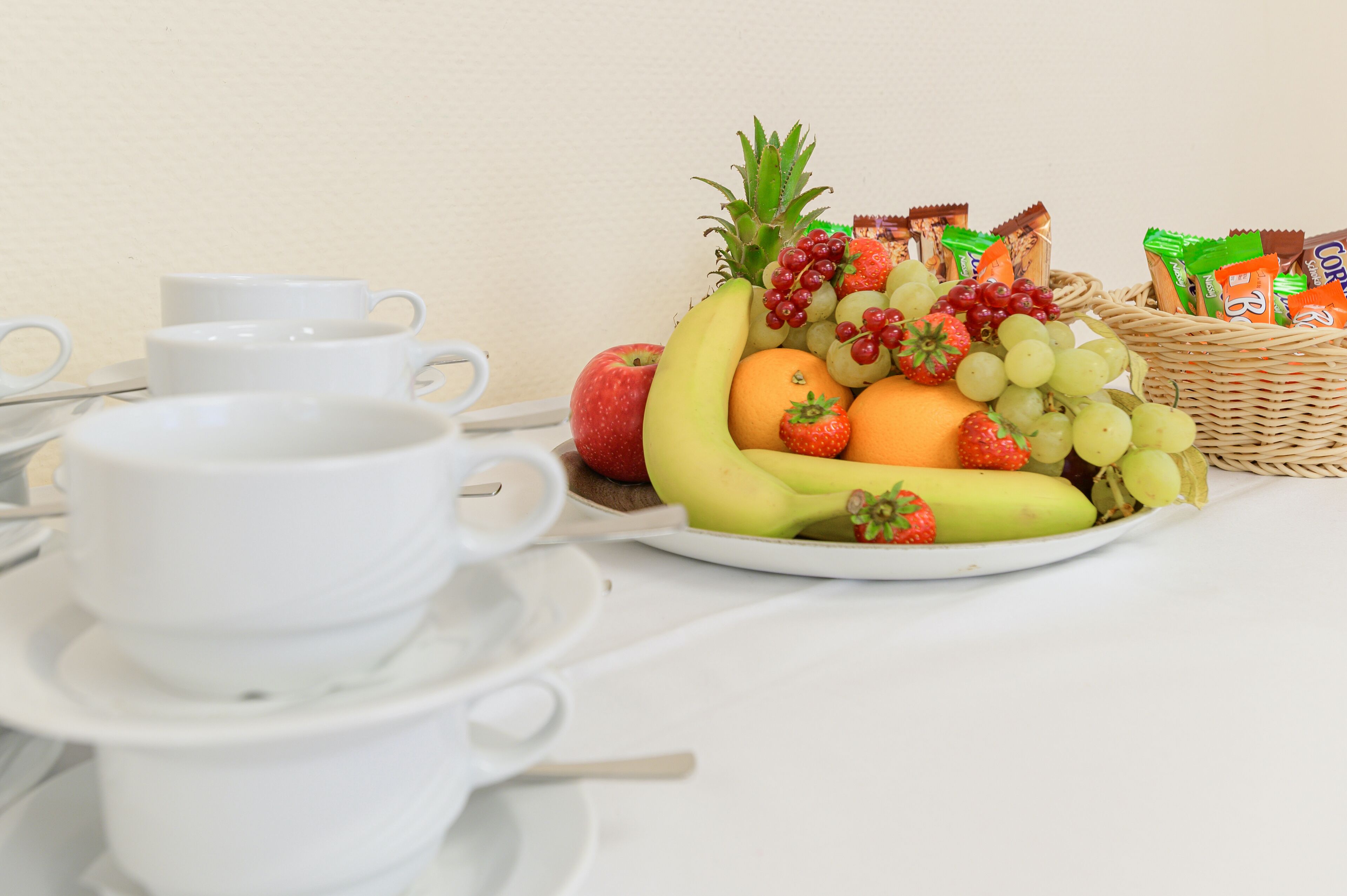Una mesa de desayuno con una bandeja de frutas, tazas de café y una cesta de mimbre con aperitivos.
