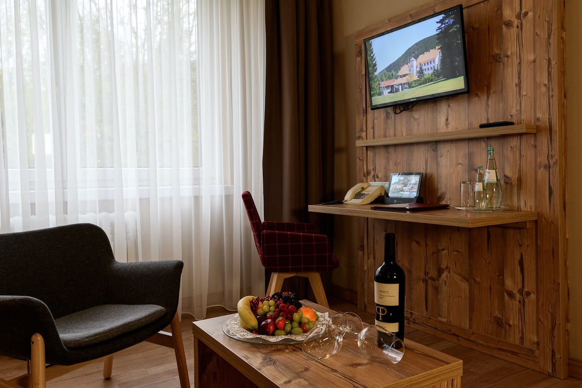 A wooden interior with a television mounted on the wall, a dining table with a fruit bowl, a bottle of wine, and a red chair.