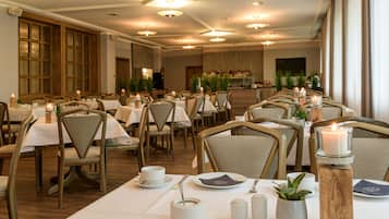 A restaurant with multiple tables set with white tablecloths, candles, and a variety of tableware.