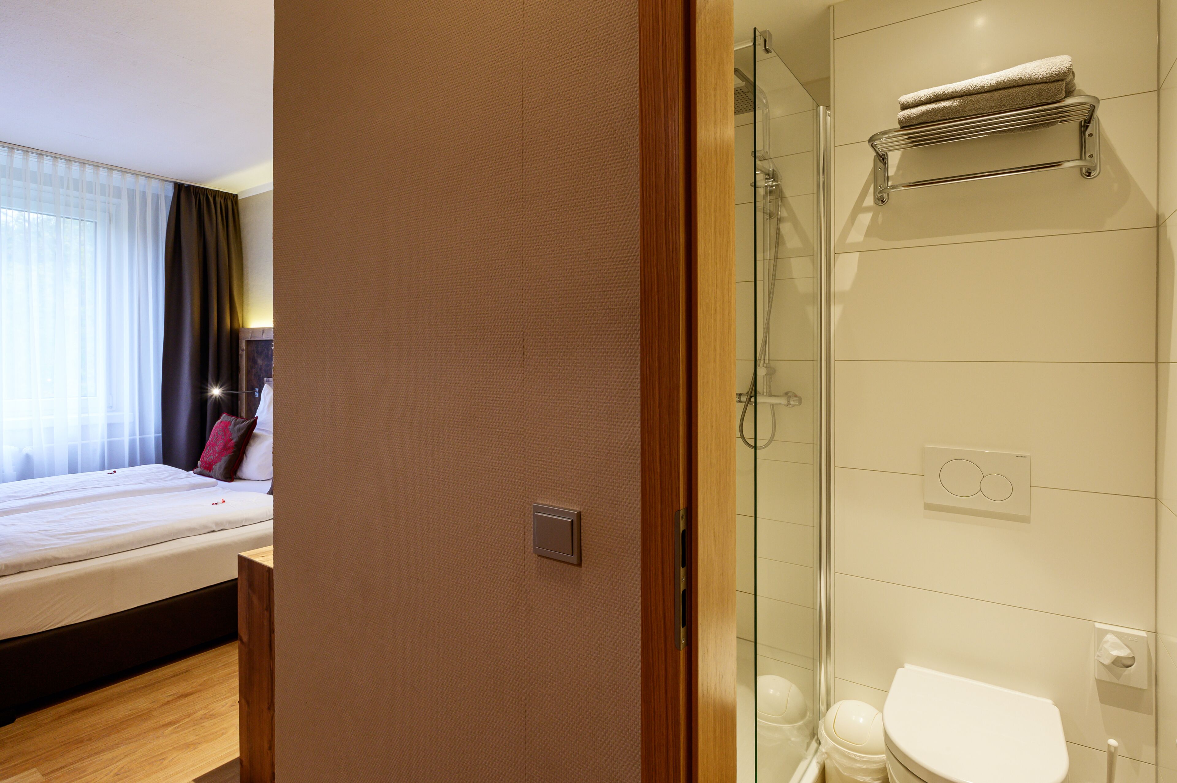 Una habitación de hotel con cama, baño con cabina de ducha de vidrio y un perchero para toallas.