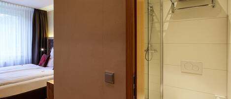 A hotel room with a bed, a bathroom with a glass shower enclosure, and a towel rack.