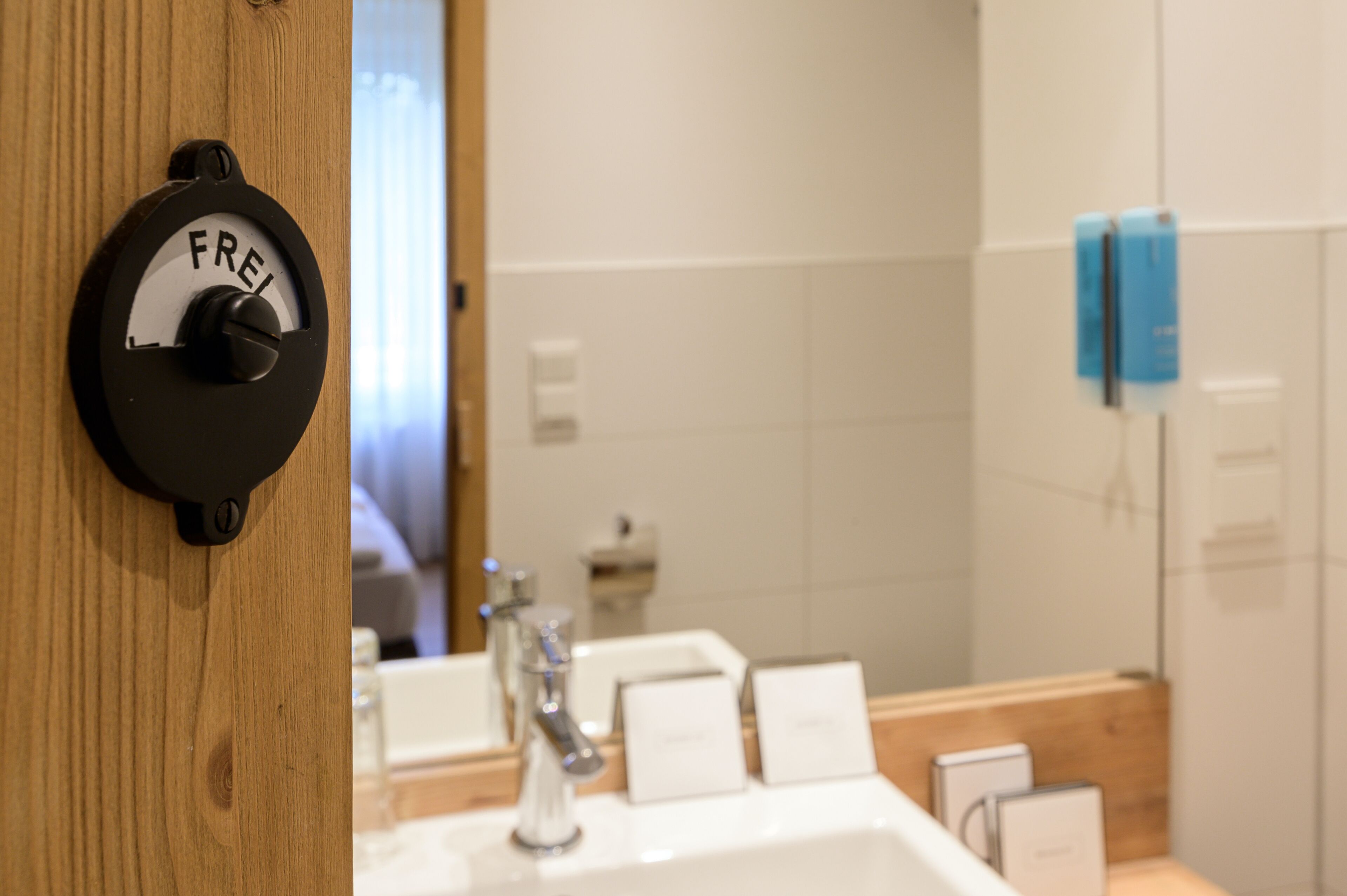 Une salle de bain avec une porte en bois, un lavabo blanc et un miroir.