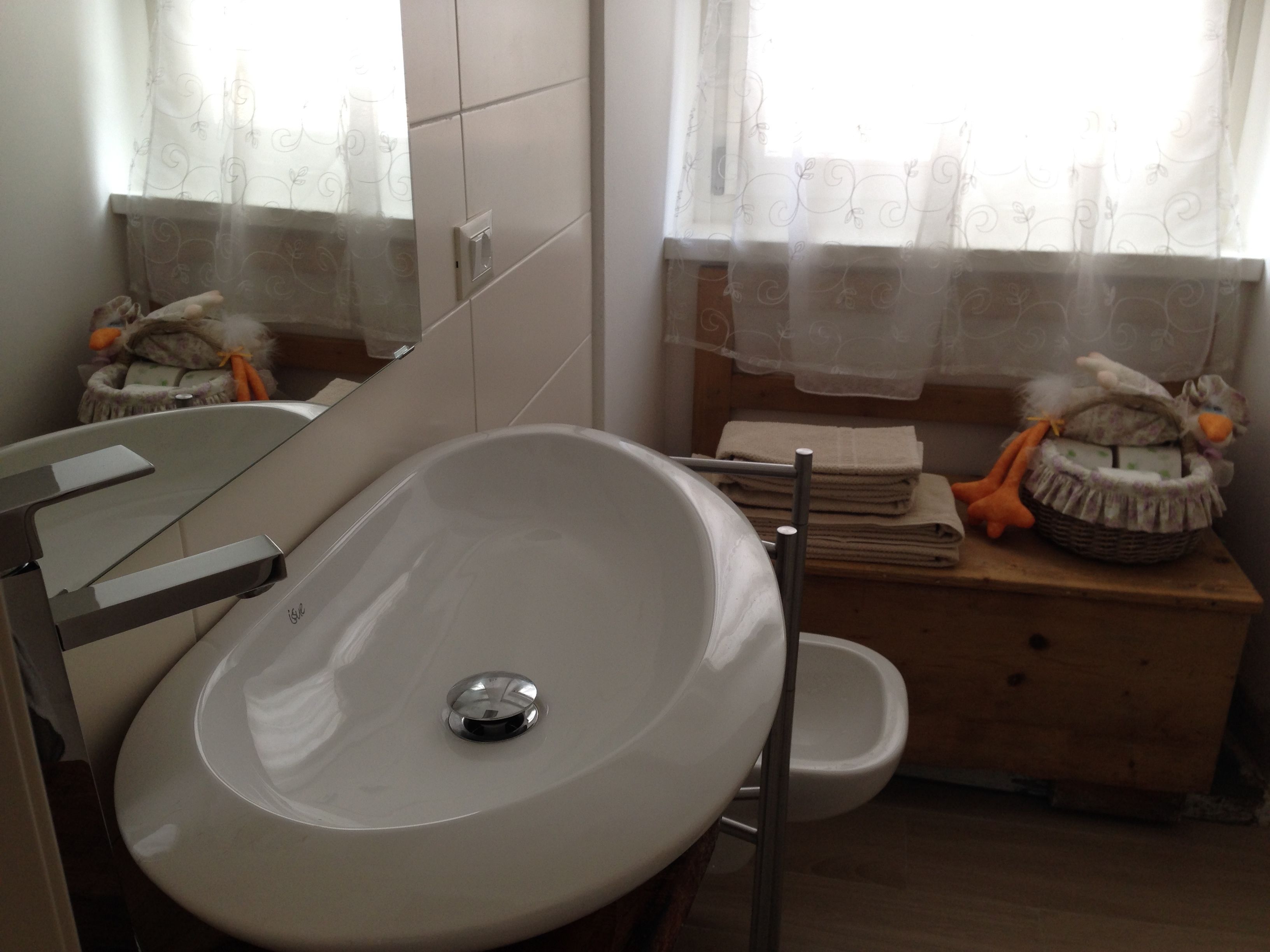 A bathroom with a white sink, a mirror, a toilet, and a vanity with a basket of toiletries.