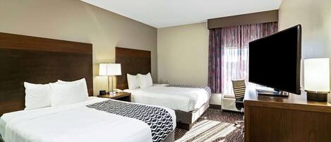 A hotel room with two beds, a flat-screen TV, a desk with a lamp, and a patterned rug.