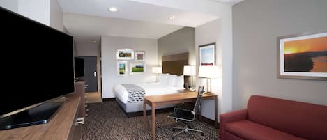 A hotel room with a bed, a desk with a computer, a TV, a red sofa, and a patterned carpet.