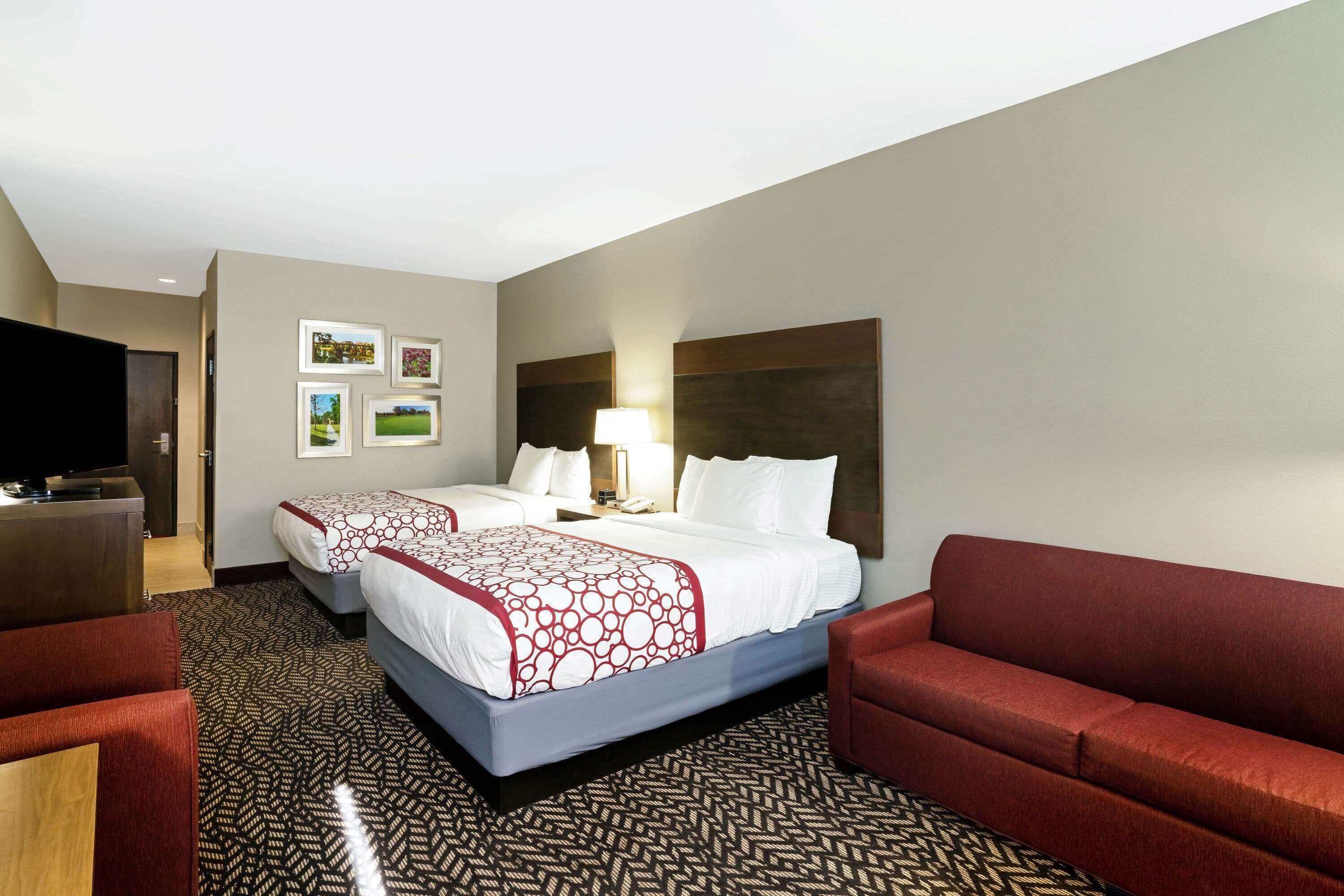 A hotel room with two beds, a desk, a TV, and a red sofa.